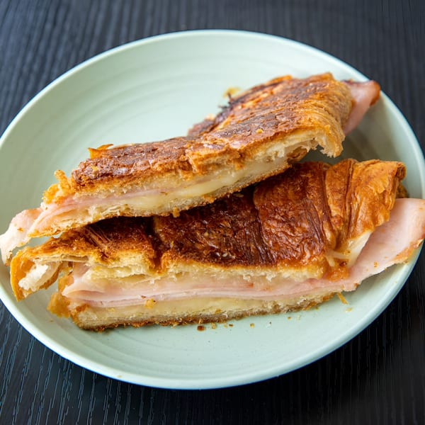 Two halves of a Cuban ham and cheese croissant sandwich on a light green plate.