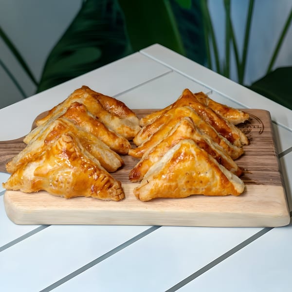 Golden brown Cuban pastelitos, triangular pastries with a glossy finish, arranged on a wooden board.